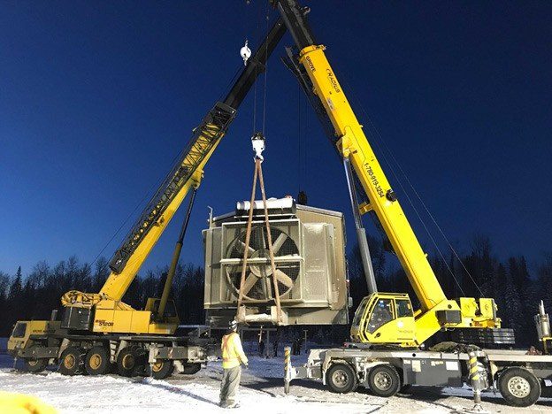 Tandem crane lift setting a compression module into place at an Alberta site in winter