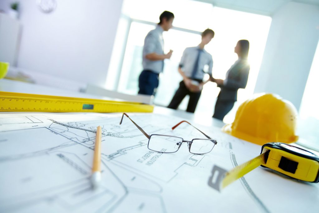 Engineering drawings, hard hat and drafting tools on a desk during EPCM project planning